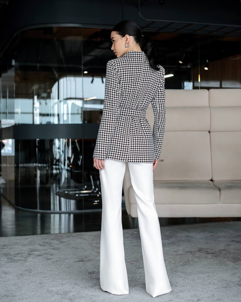 Person wearing a black and white checkered blazer and white pants in an indoor setting.