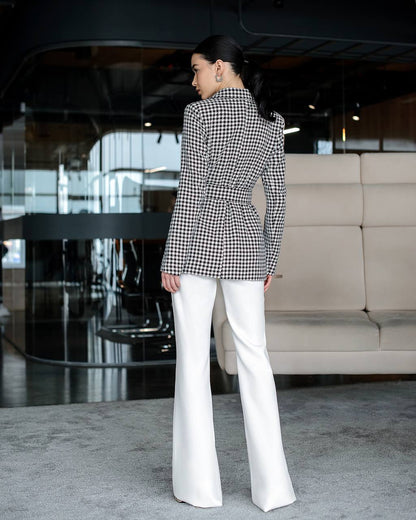 Person wearing a black and white checkered blazer and white pants in an indoor setting.