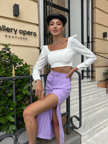 Woman in a white top and purple skirt posing on steps in front of 'Gallery Opera Boutique'.