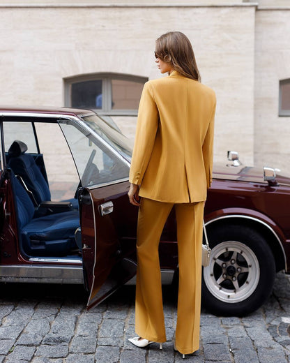 Woman in a mustard yellow suit standing next to an open car door on a street.
