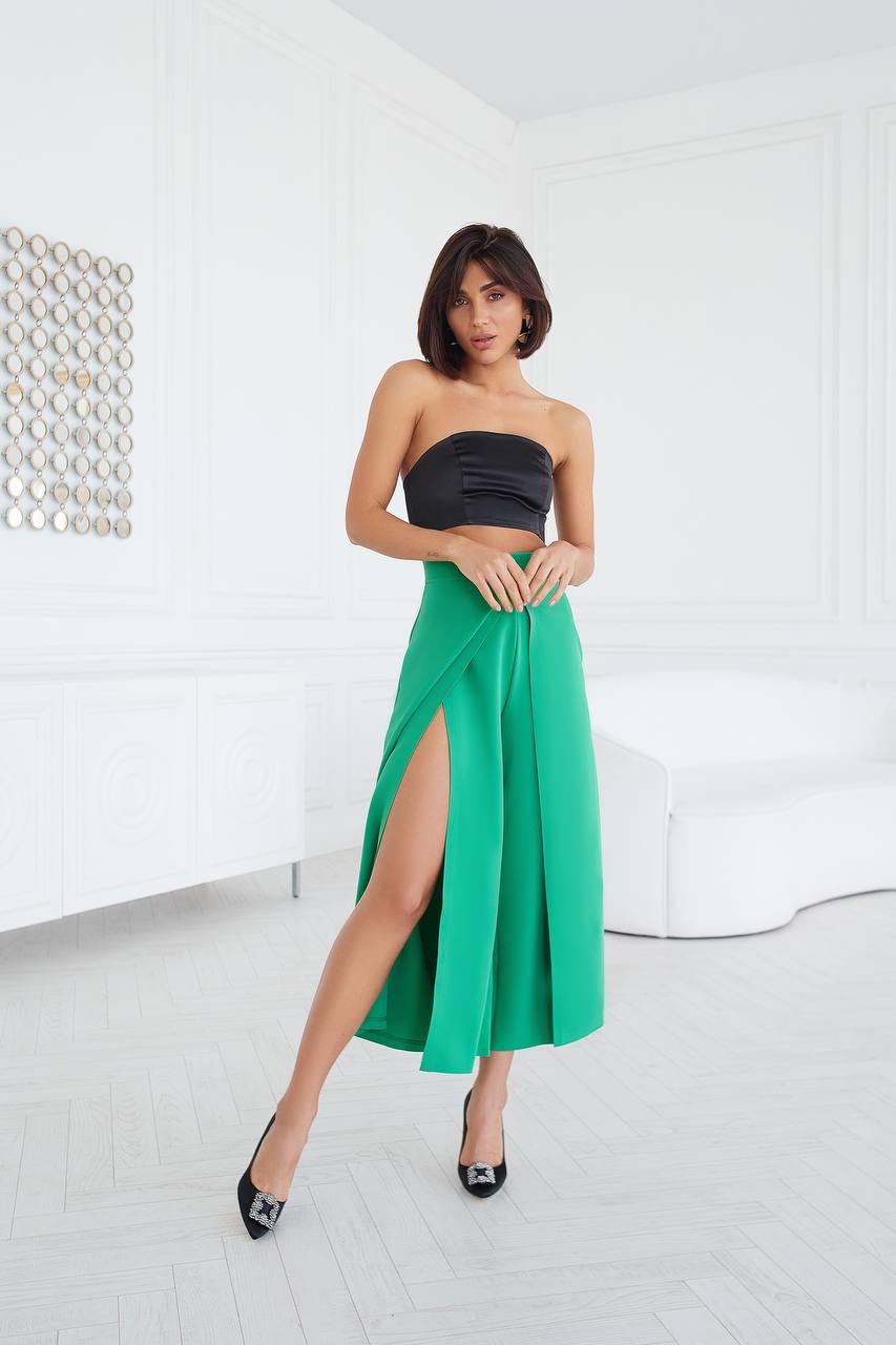 Woman wearing a strapless black top and green skirt in a minimal white room.