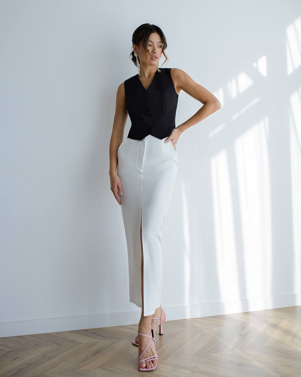 Woman wearing a black sleeveless top and white pants in a bright room.