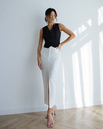 Woman wearing a black sleeveless top and white pants in a bright room.
