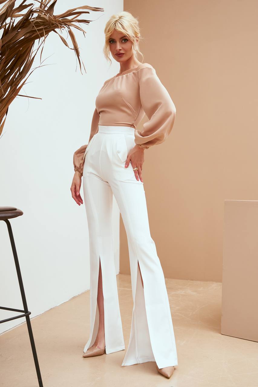 Woman wearing a beige top and white pants in a minimalistic setting