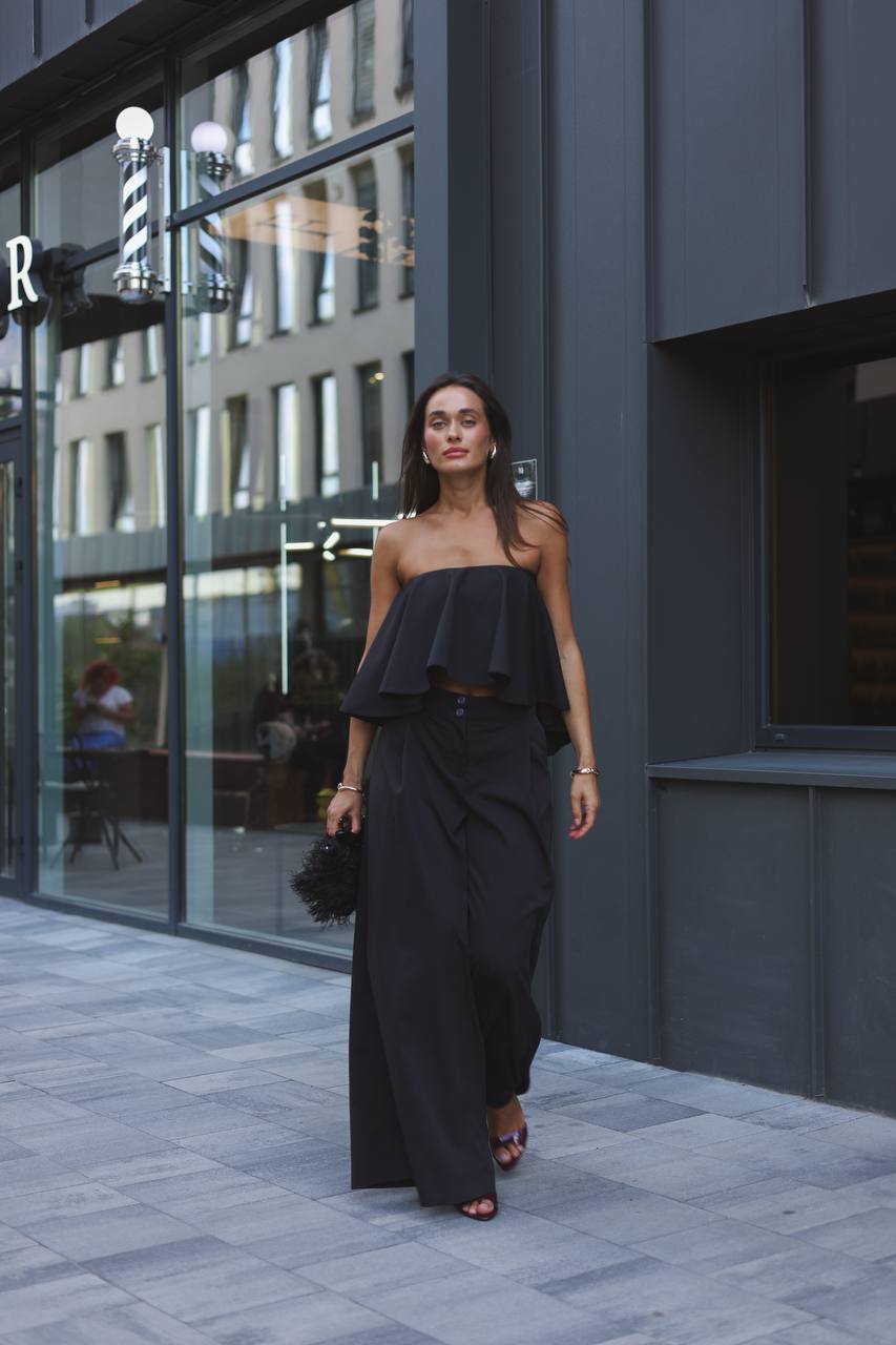 Woman in a black strapless top and long skirt walking on a city street.