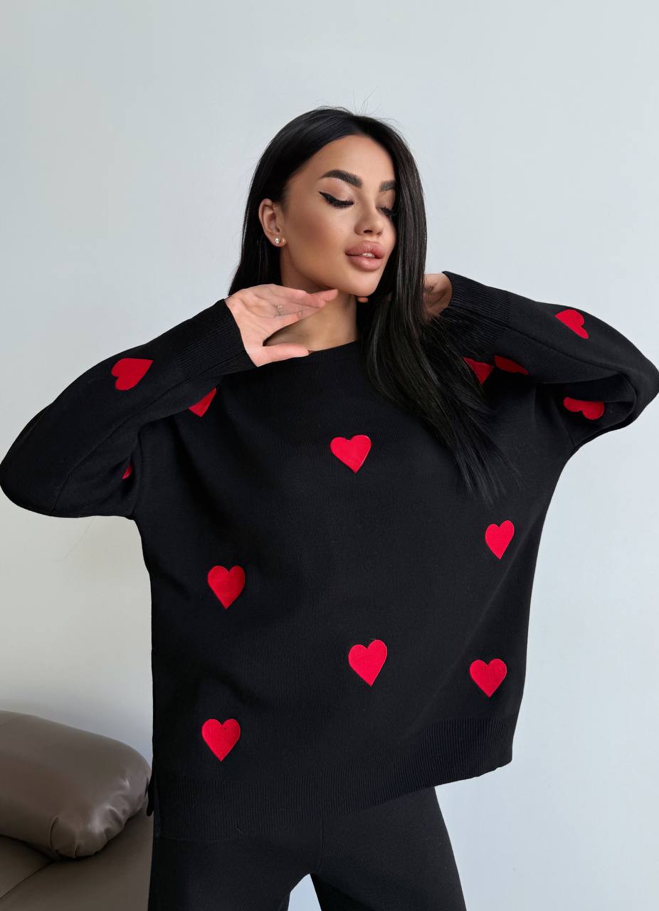 Woman wearing a black sweater with red heart patterns against a light gray background