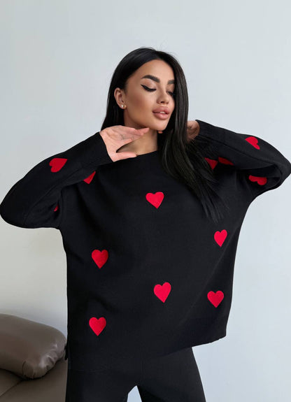 Woman wearing a black sweater with red heart patterns against a light gray background