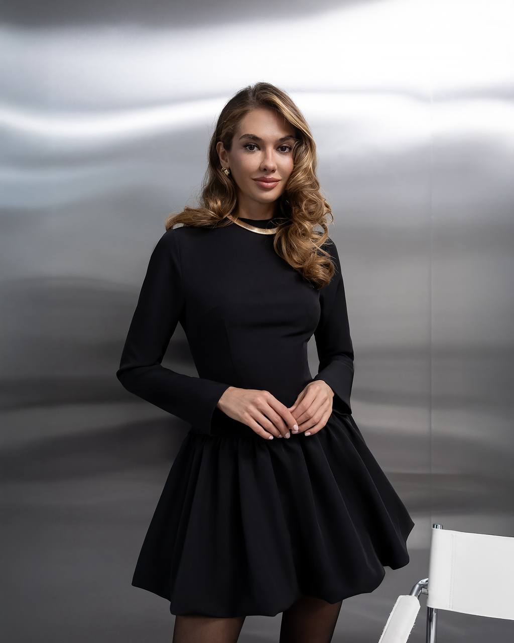 Woman wearing a black dress standing against a metallic background