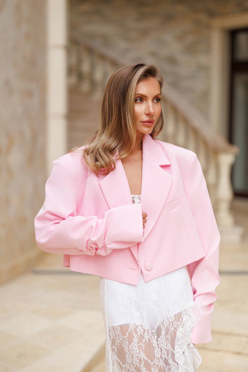 Woman wearing a pink blazer over a white outfit in an outdoor setting