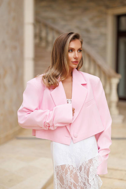 Woman wearing a pink blazer over a white outfit in an outdoor setting