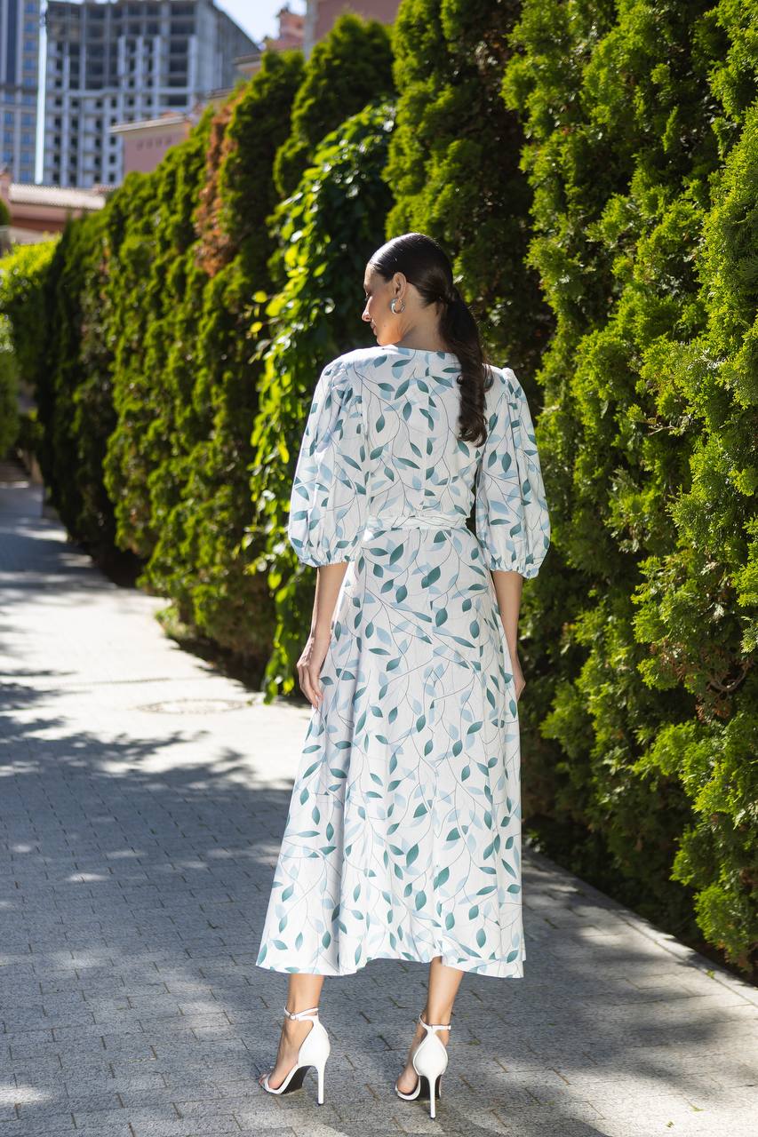 Woman in a light blue dress with green leaf pattern walking on a sidewalk.