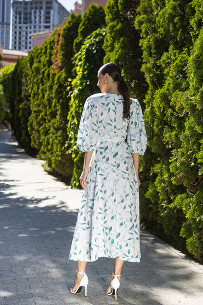 Woman in a light blue dress with green leaf pattern walking on a sidewalk.