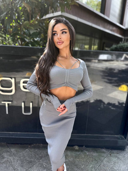 Woman in a gray outfit standing in front of a building entrance.