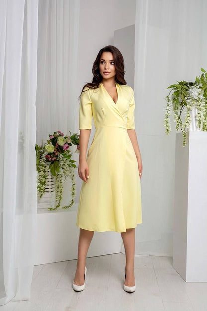 Woman wearing a yellow dress standing in a bright room with white walls and plants.