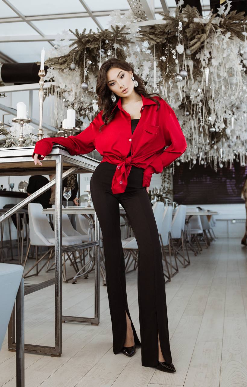 Woman in a red jacket and black pants standing in an elegant indoor setting with decorative elements.