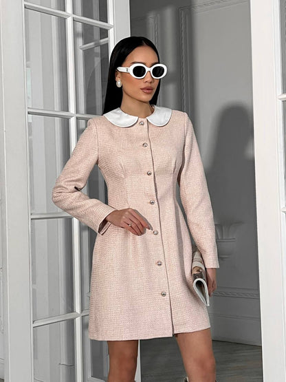 Woman wearing a light pink coat with a white collar in a neutral setting
