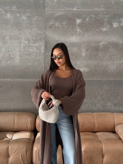 Woman holding a handbag against a gray wall with a brown couch.