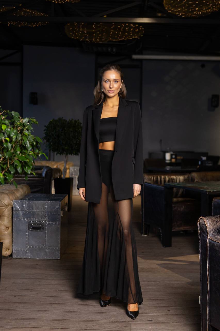 Woman in a black outfit standing in a dimly lit room with plants and furniture.