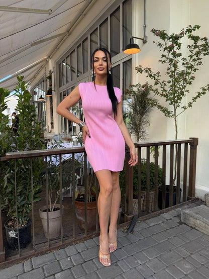 Woman in a pink dress standing on a patio with plants and a building in the background
