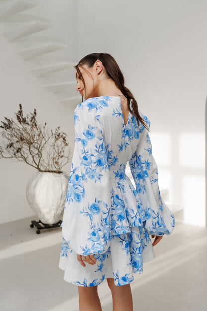 Woman wearing a white dress with blue floral patterns in a bright room.