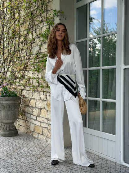 Woman in white outfit standing in front of a stone wall and glass door.