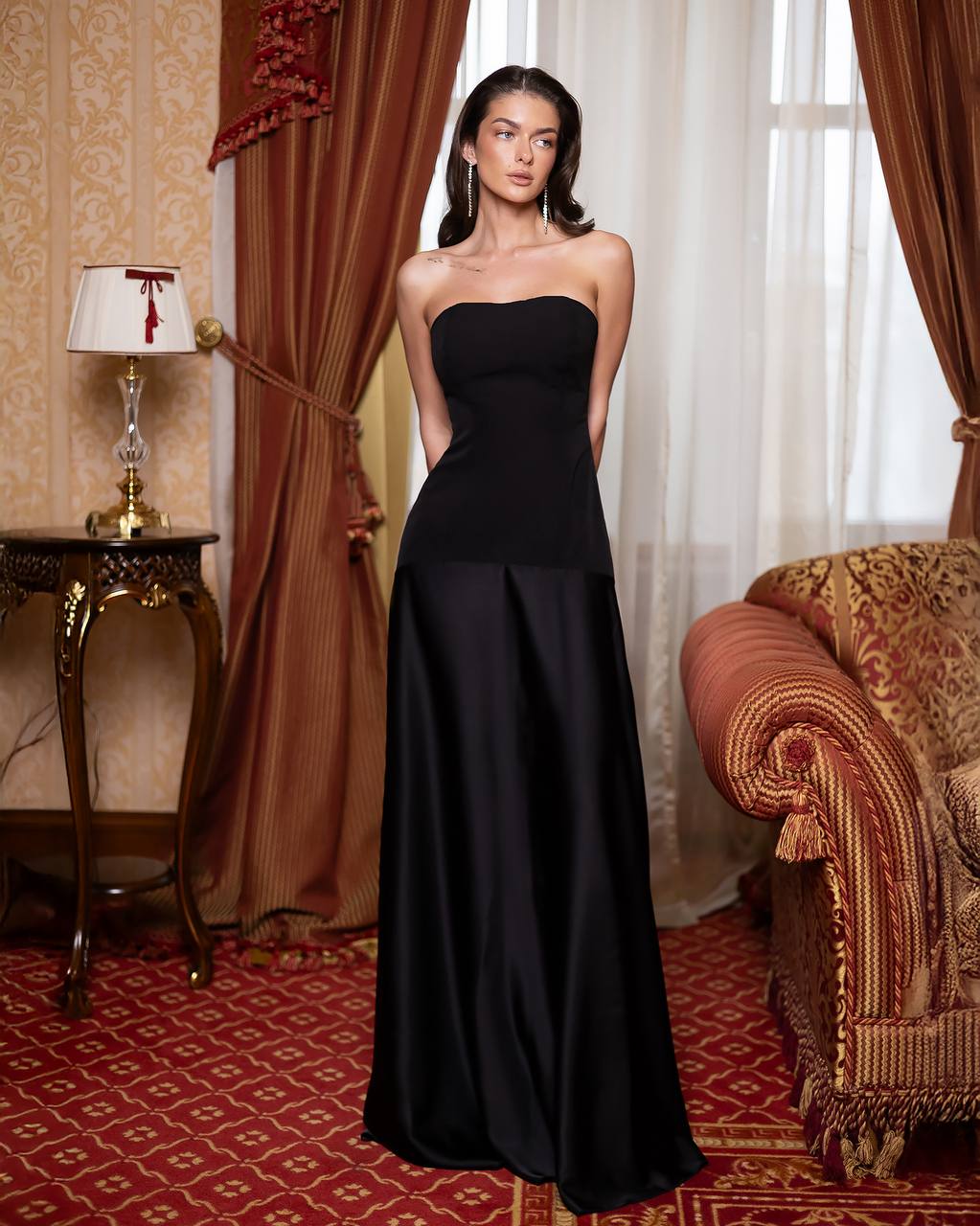 Woman in a black strapless gown standing in an elegant room with red and gold decor.