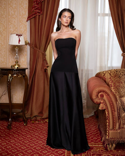 Woman in a black strapless gown standing in an elegant room with red and gold decor.