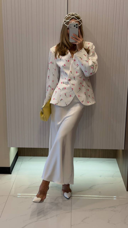 Person wearing a white floral blouse and white pants with a yellow handbag, standing in a hallway.