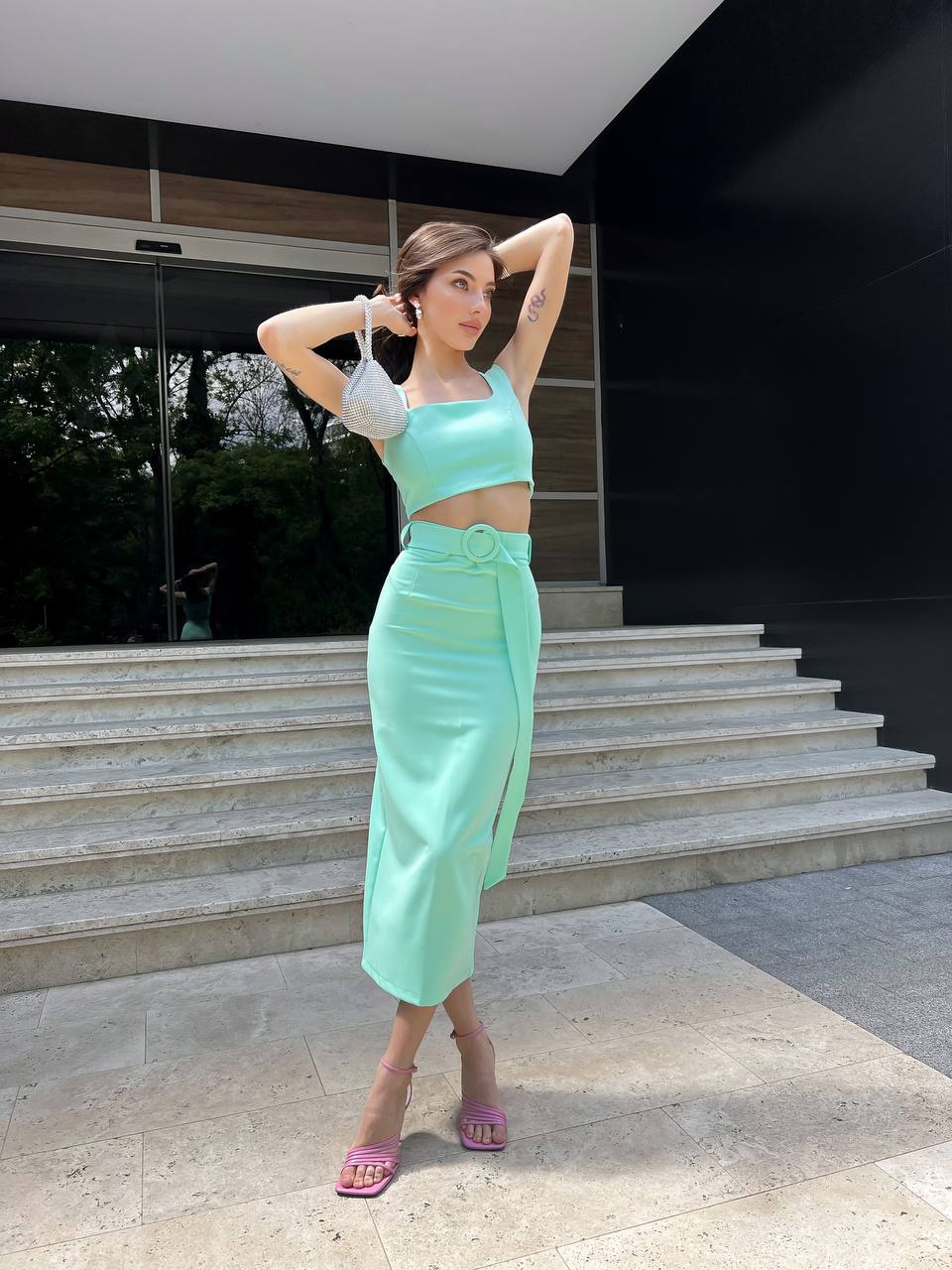 Woman in a light green outfit posing on steps outside a modern building.