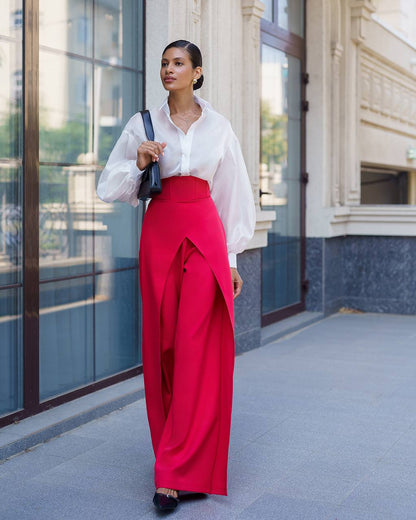 Woman wearing a white blouse and red pants standing in front of a building.