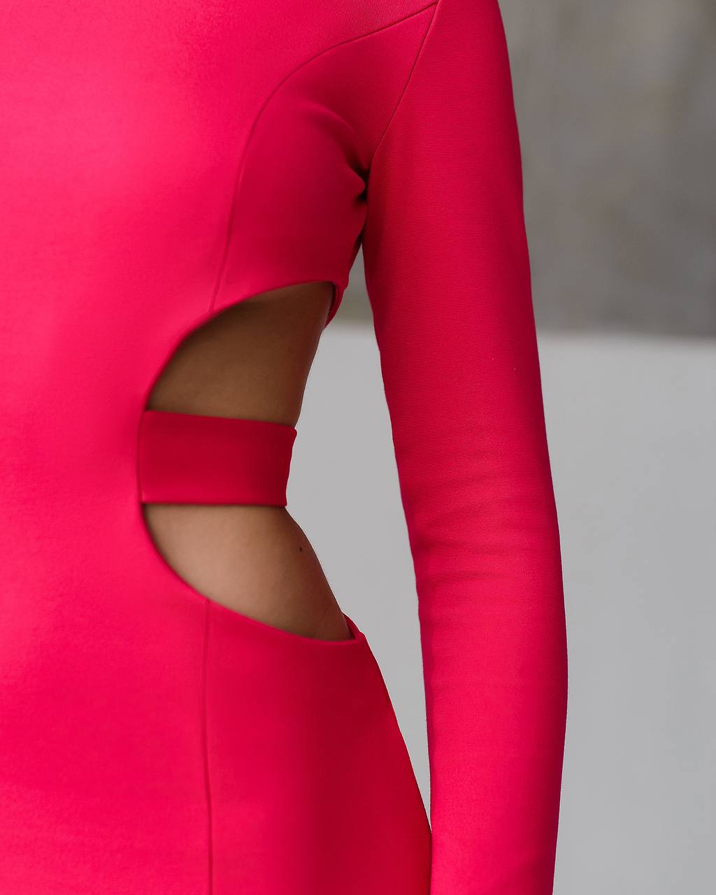 Close-up of a bright pink long-sleeve top with cut-out design on a neutral background