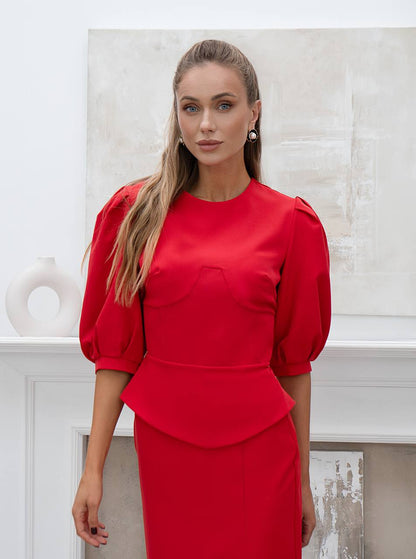 Woman wearing a red dress with puffed sleeves against a white wall.