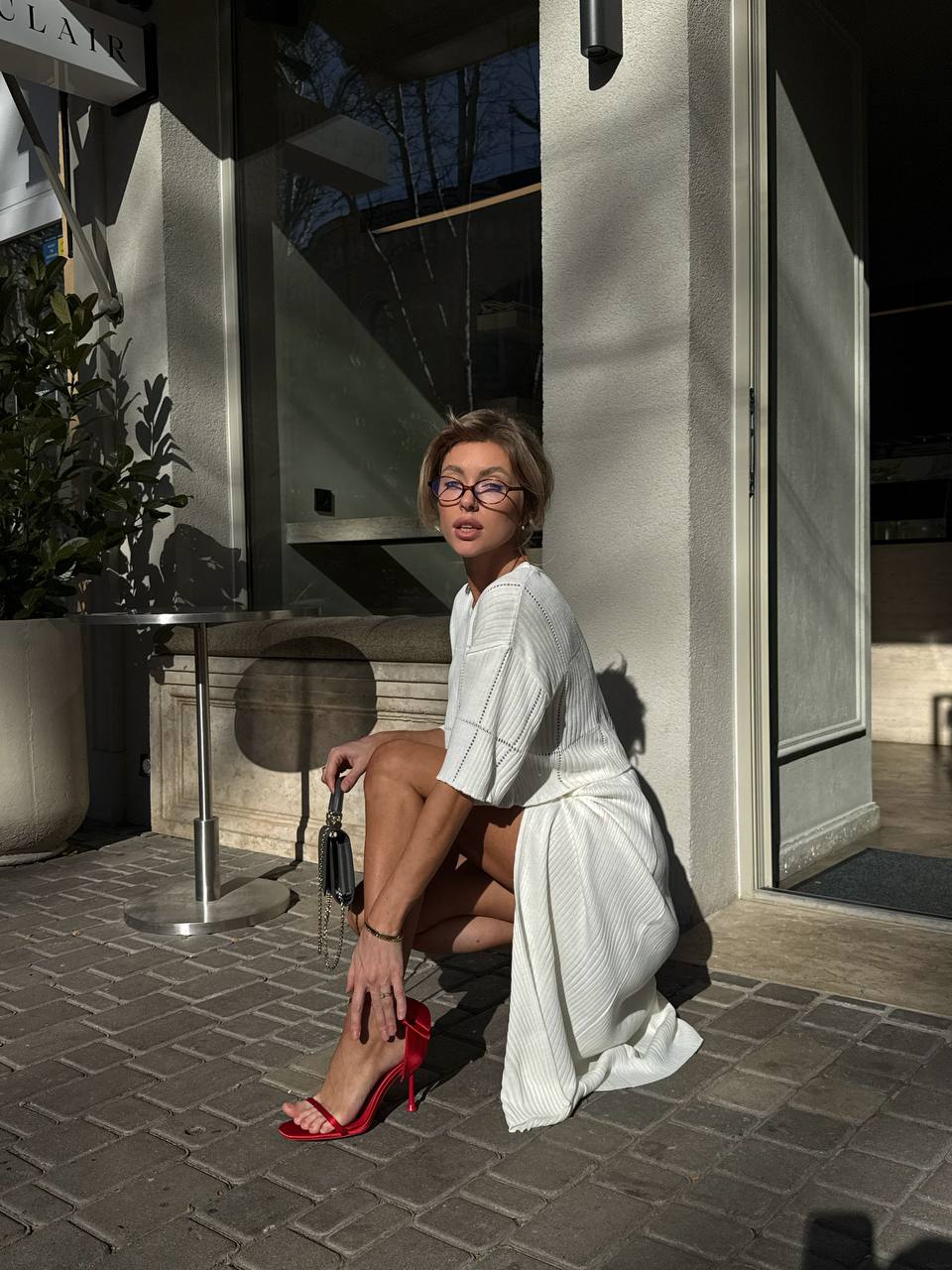 Woman in a white outfit with red shoes sitting on a stone pavement.