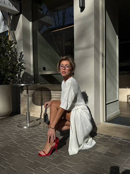Woman in a white outfit with red shoes sitting on a stone pavement.