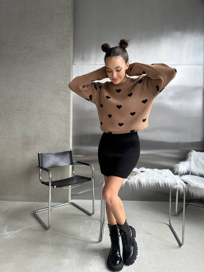 Woman wearing a brown sweater with black heart patterns and a black skirt in a room.