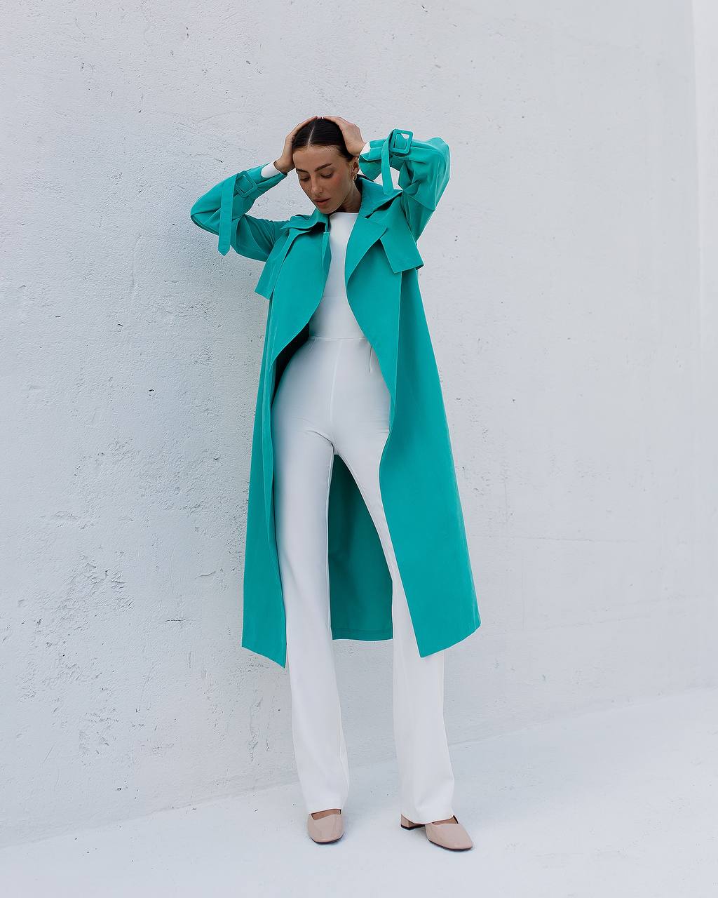 Person wearing a turquoise coat over a white outfit against a light gray background