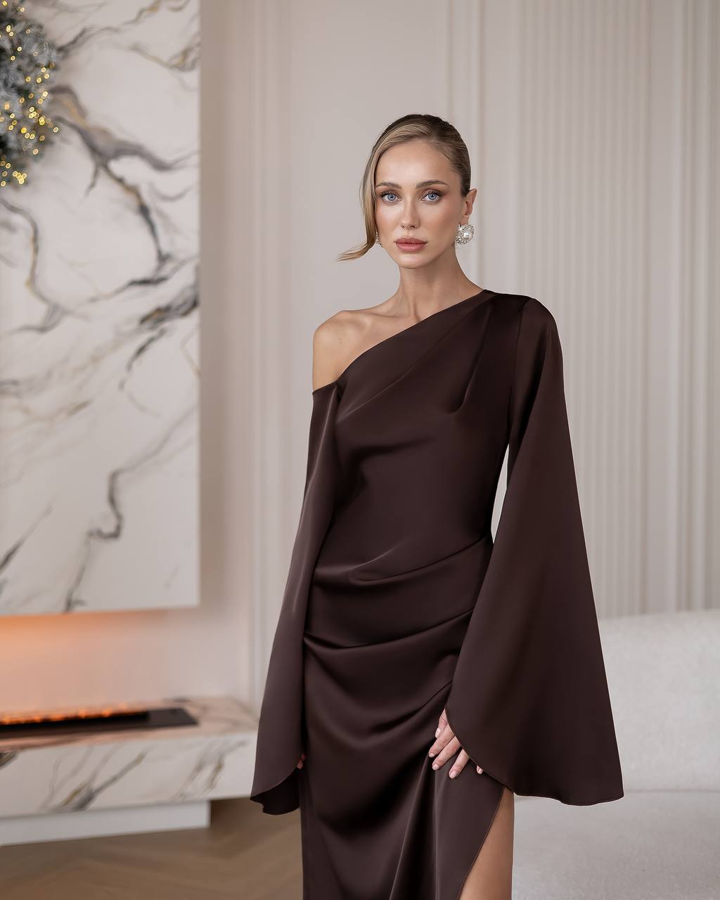 Woman wearing a brown one-shoulder dress in an elegant indoor setting.