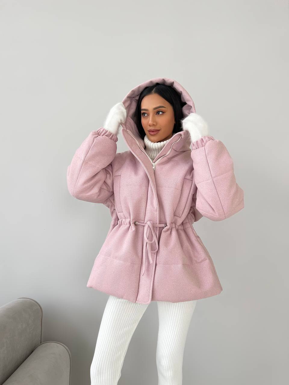 Person wearing a pink hooded coat with white gloves against a plain background