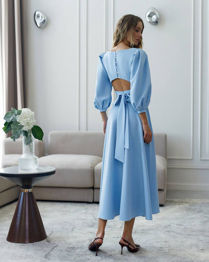 Woman wearing a light blue dress with a cutout back in an elegant room.