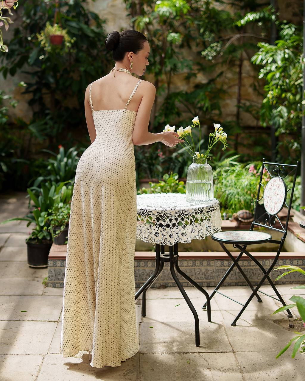 Woman in a long white dress standing by a table with flowers in an outdoor setting