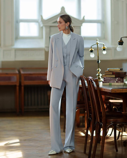 Woman in a gray suit standing in a room with wooden furniture and large windows.