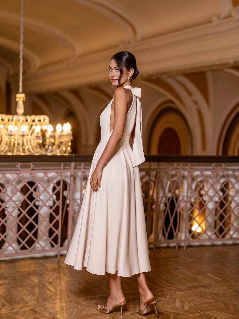 Woman in a white dress standing in an elegant indoor setting with chandeliers.