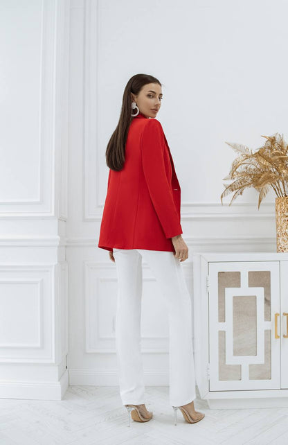 Woman wearing a red blazer and white pants in a room with decorative elements.