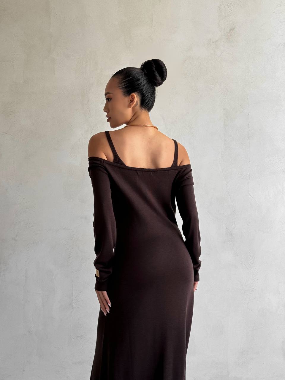 Woman wearing a dark brown off-shoulder dress against a plain background