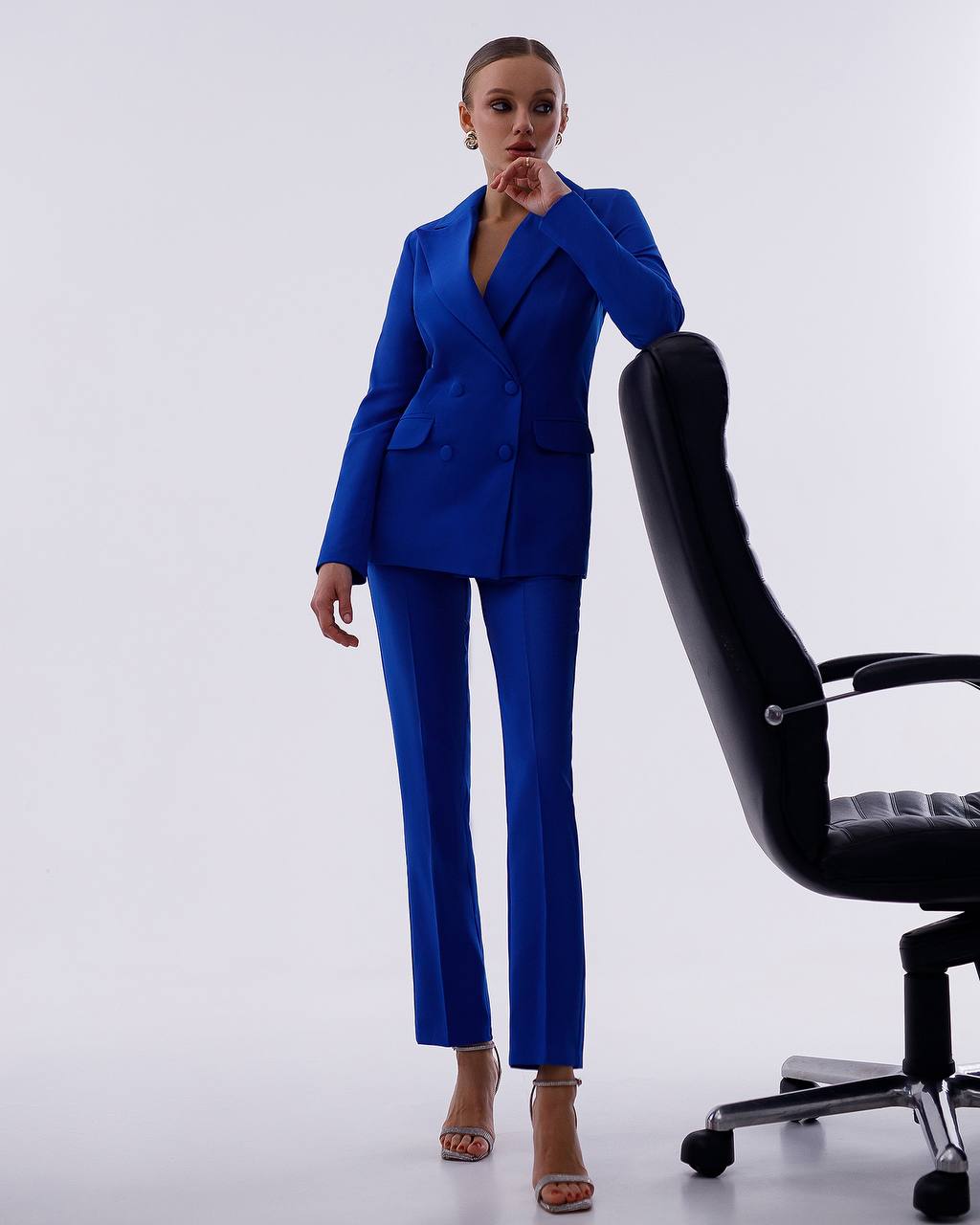 Woman in a blue suit standing next to a black office chair on a white background