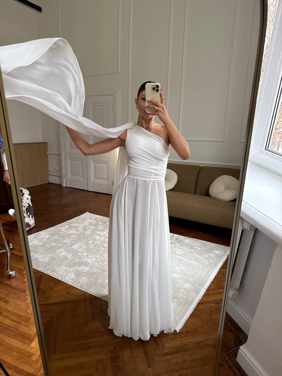 Person wearing a white dress in a room with wooden flooring and a mirror.