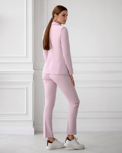 Woman wearing a pink suit standing against a white wall.