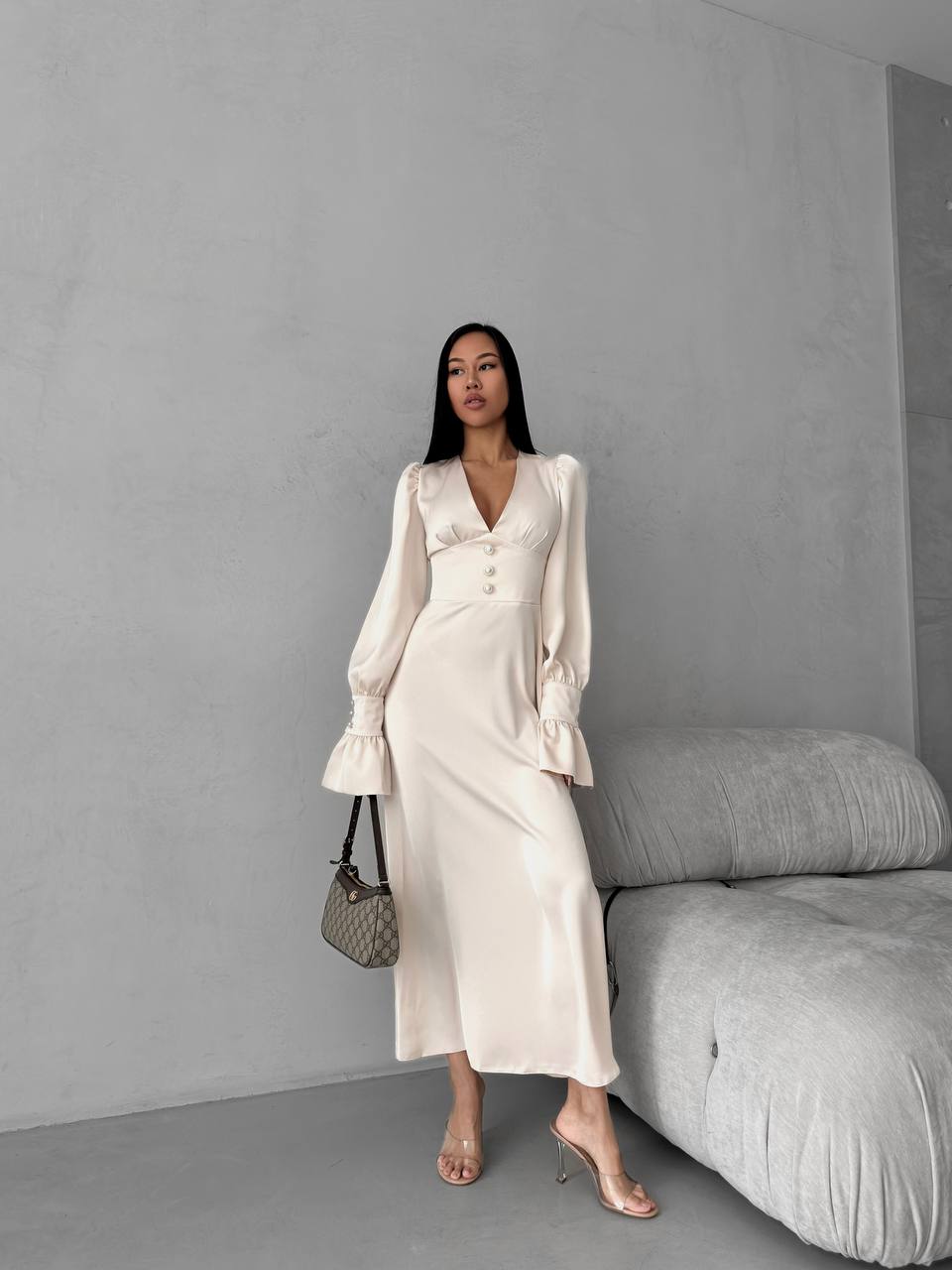 Woman in a white outfit standing against a gray wall with a gray sofa.