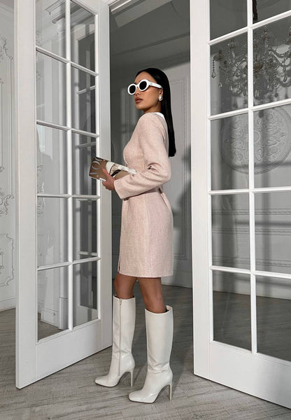 Woman in a pink dress and white knee-high boots standing in front of glass doors.