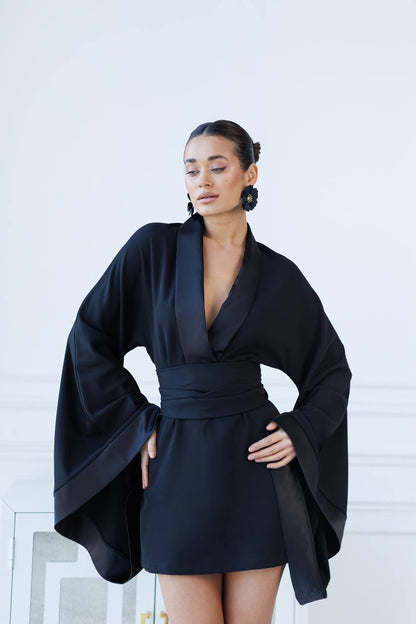 Woman wearing a black dress with a cape-like design against a white background